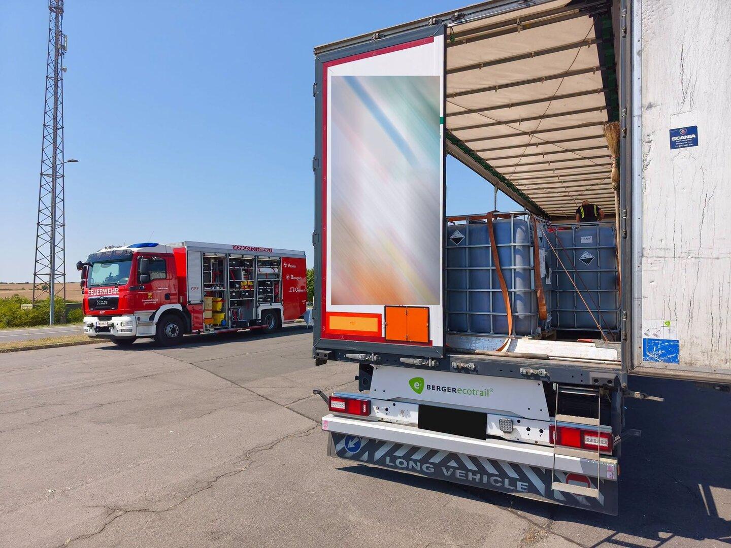 Feuerwehrwagen neben einem offenen Lkw mit IBC-Behältern an einer Landstraße.