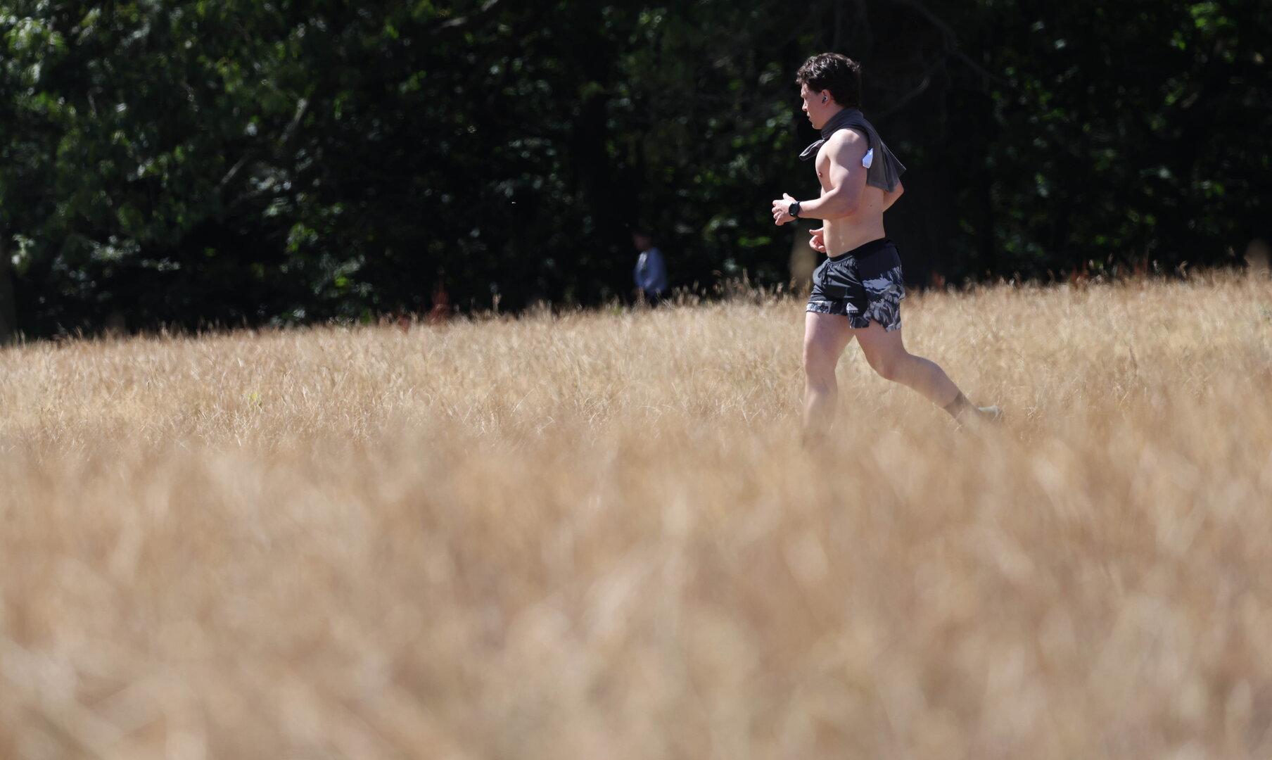 Ein barfüßiger Mann joggt durch ein trockenes Grasfeld vor dunklem Wald.