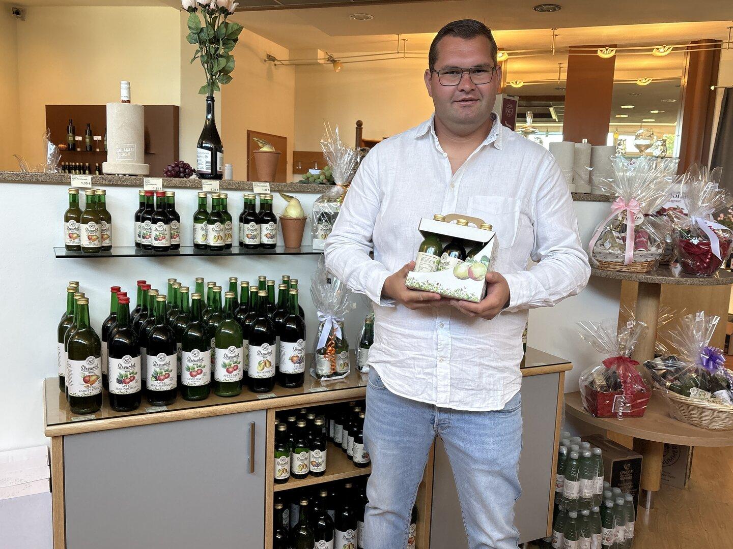 Saftproduzent Martin Trummer weißem Hemd hält eine Geschenkbox mit Flaschen in einem Laden für Getränke und Geschenkkörbe.